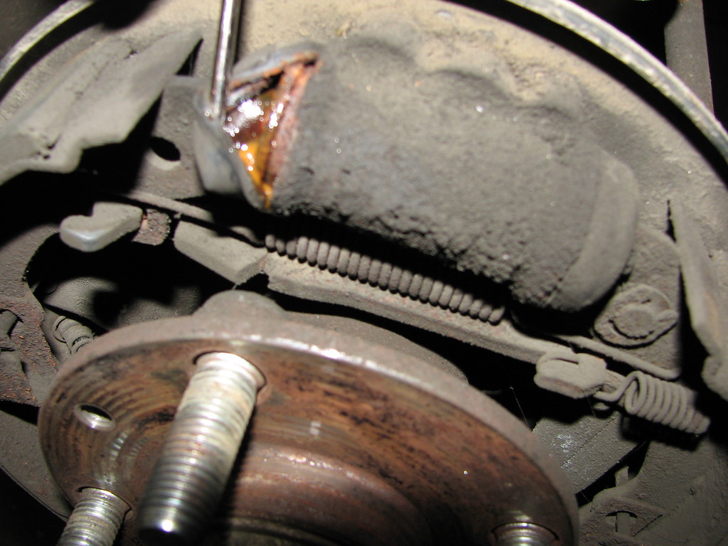 A old, dusty, and rusty Clark forklift wheel cylinder mounted in its brake plate